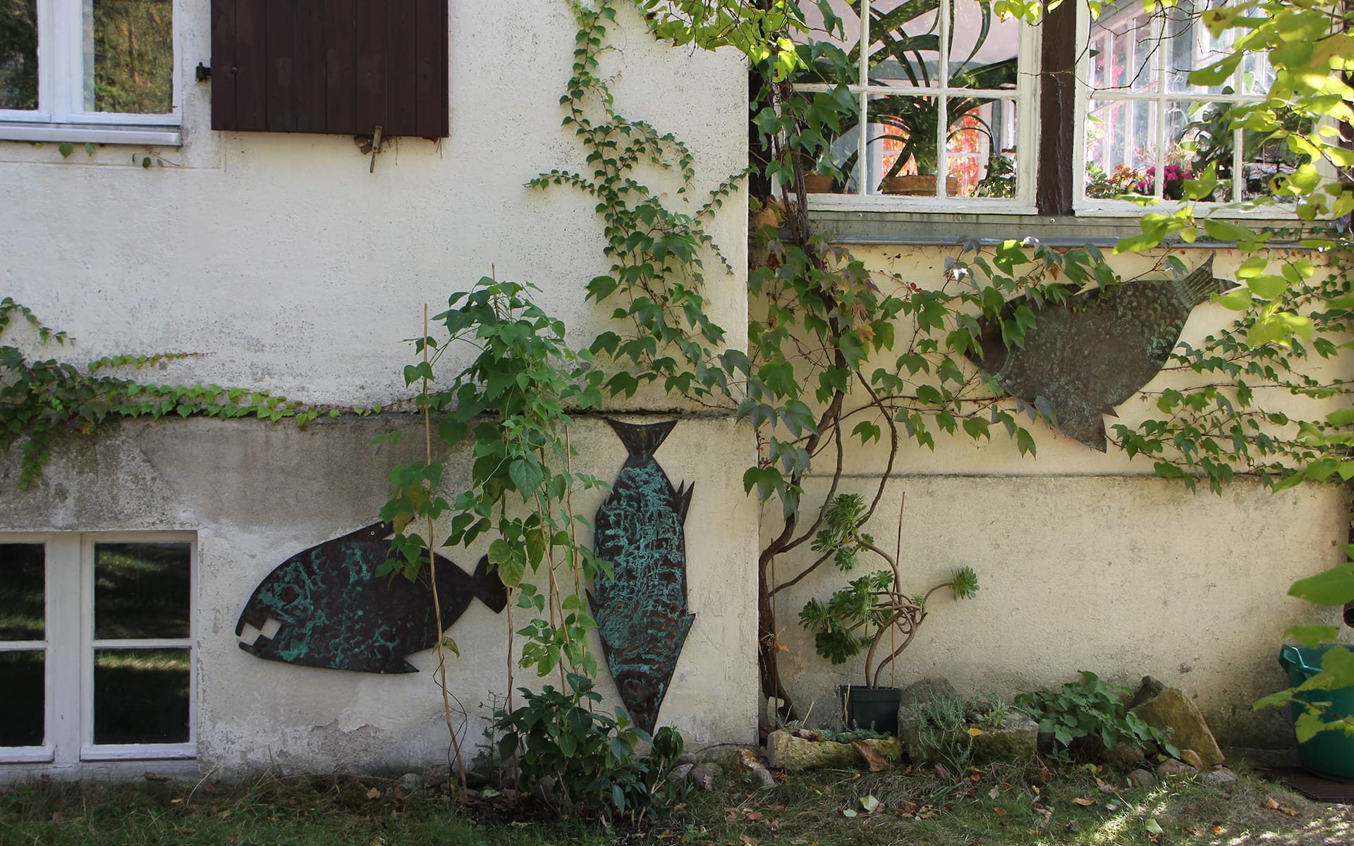 Kunsttour Stechlin - Fisch Skulpturen an der Wand im Künstlergarten